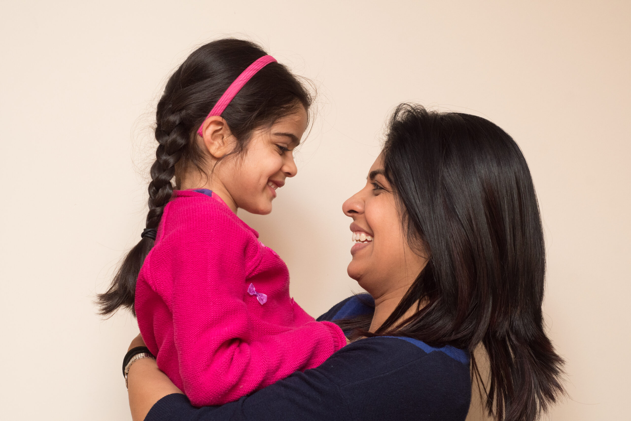 happy-mother-carrying-daughter-against-beige-background